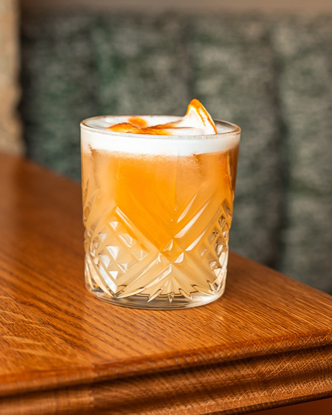 Cocktail orangé avec mousse blanche servi dans un verre taillé