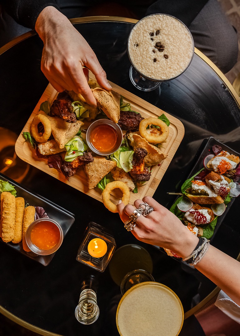 Table vue du dessus avec assiettes à partager, cocktails et mains de convives